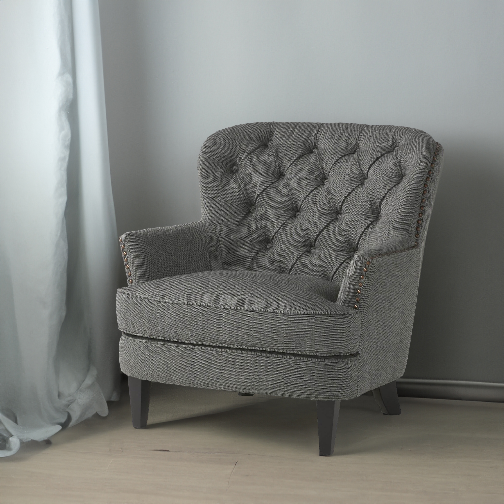 Grey club chair anchoring a styled room corner beside sheer curtains