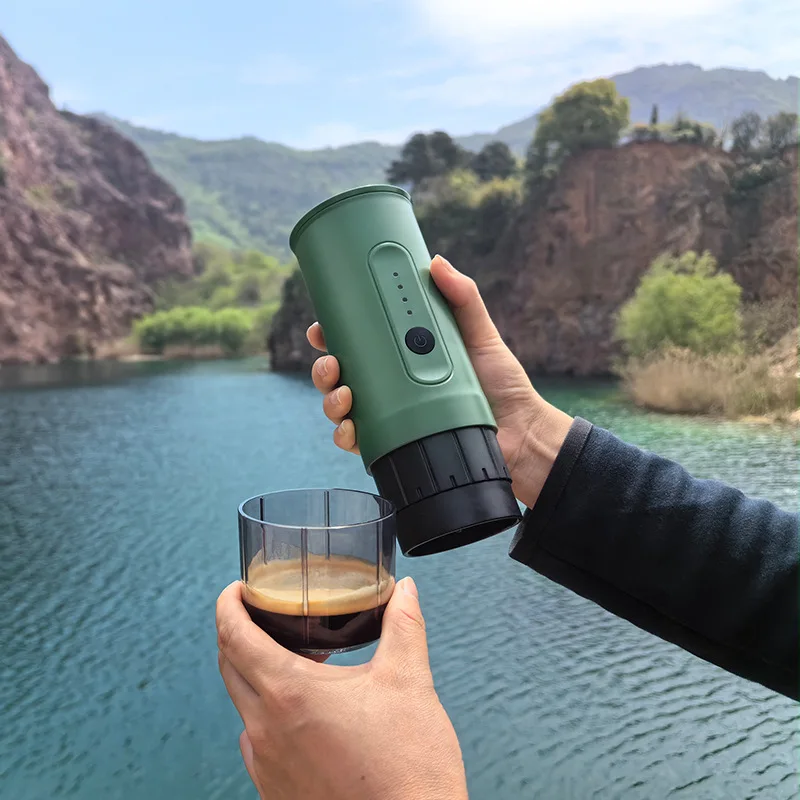 Hand holding the green espresso maker over a glass beside a mountain lake