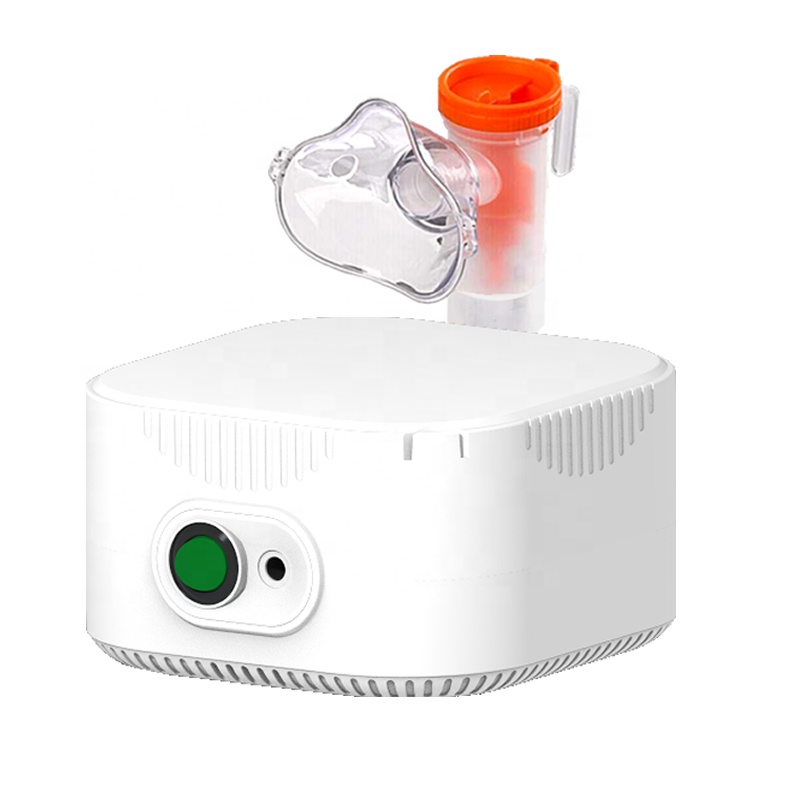 Portable electric nebulizer compressor with orange-capped medication cup and tubing, composed on light cork board with soft cotton flowers