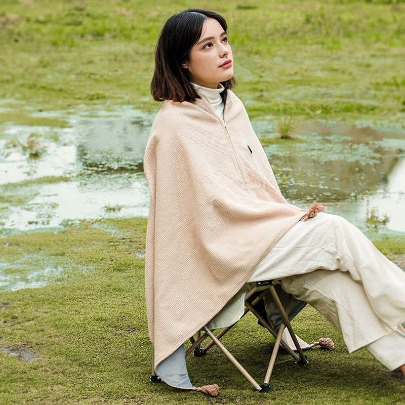 Woman seated outdoors wearing a beige heated shawl zipped at the front