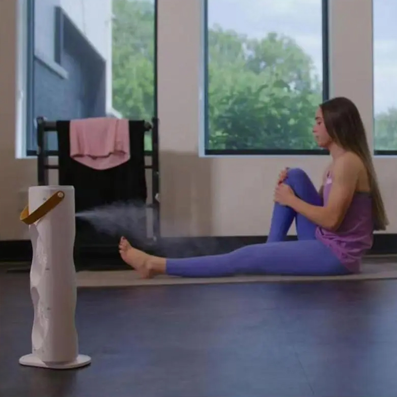 White tower cooler releasing a fine mist stream beside a woman on a yoga mat