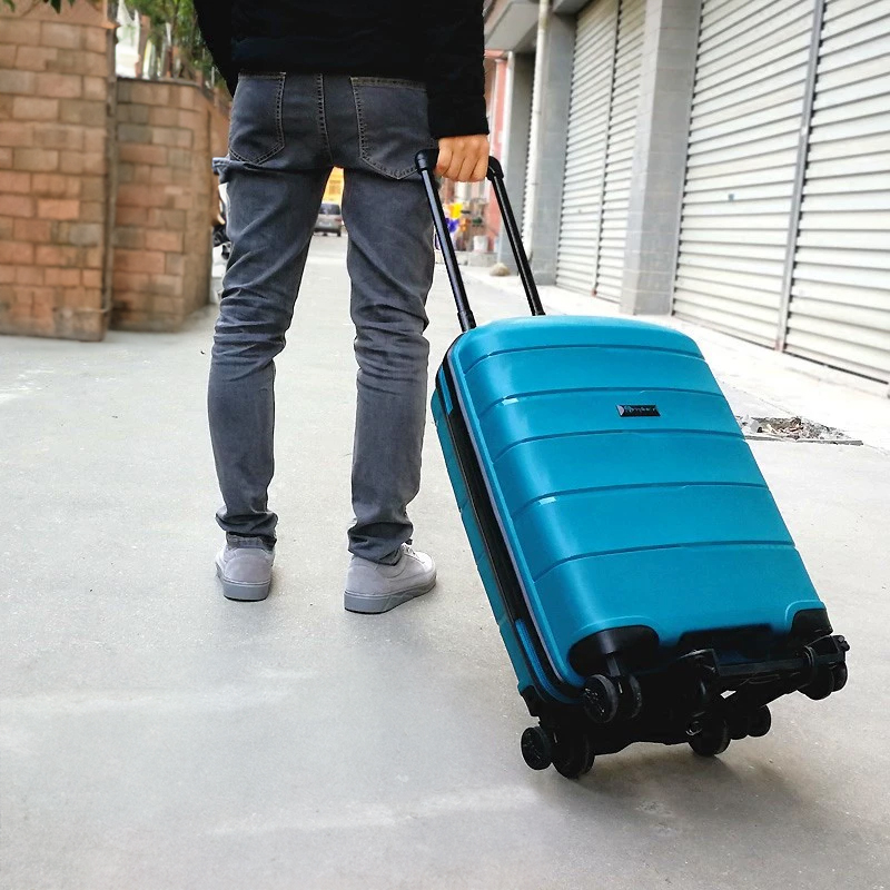 Teal hard-shell suitcase rolling on a foldable cart through a city street