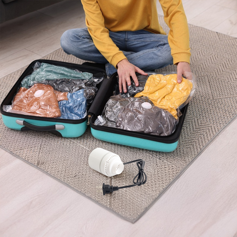 Person packing vacuum-sealed clothing bags into a suitcase beside the pump