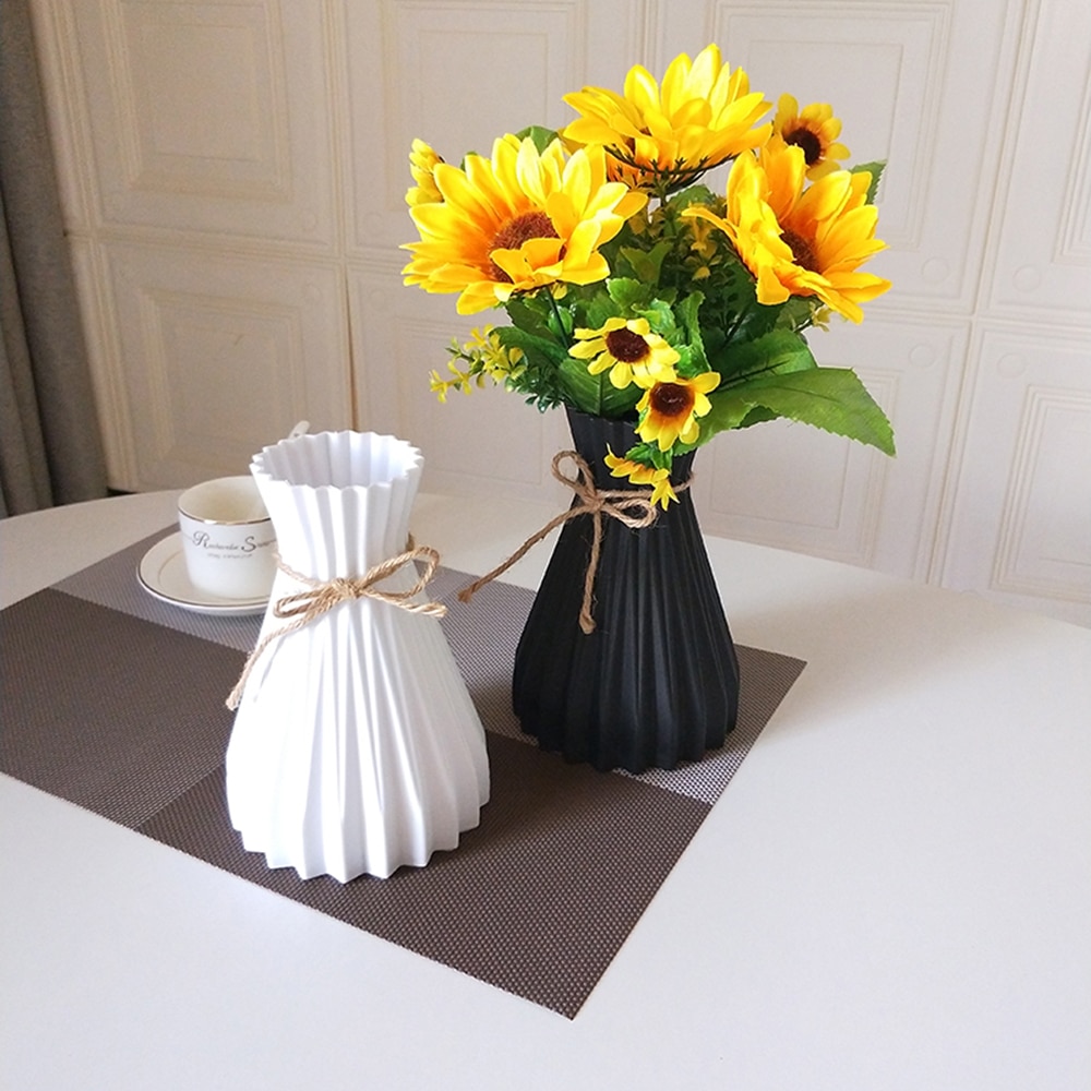 White pleated vase with jute bow beside a black vase holding sunflowers
