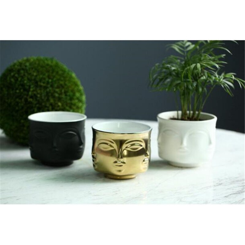 Black, gold, and white face planters on a marble table with greenery