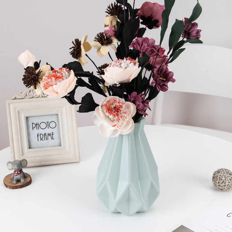 Sage faceted vase with pale peony stems on a white table