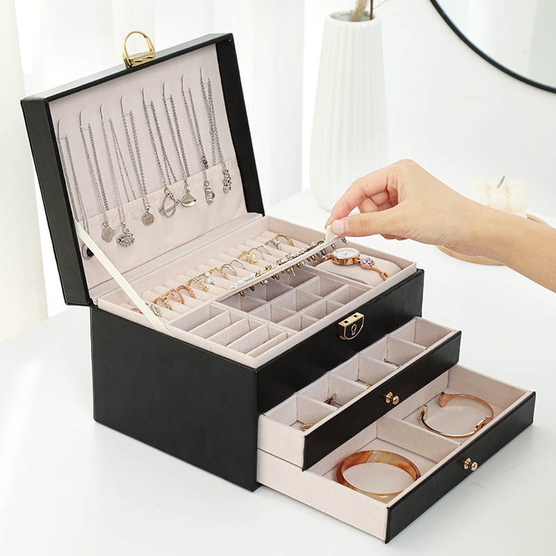 Hand placing a bracelet into an open jewelry box with necklaces hanging inside