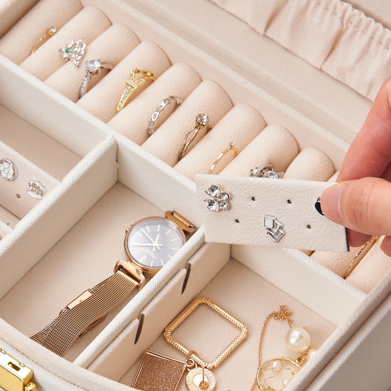 Hand lifting a removable earring card from the tray with rings inside
