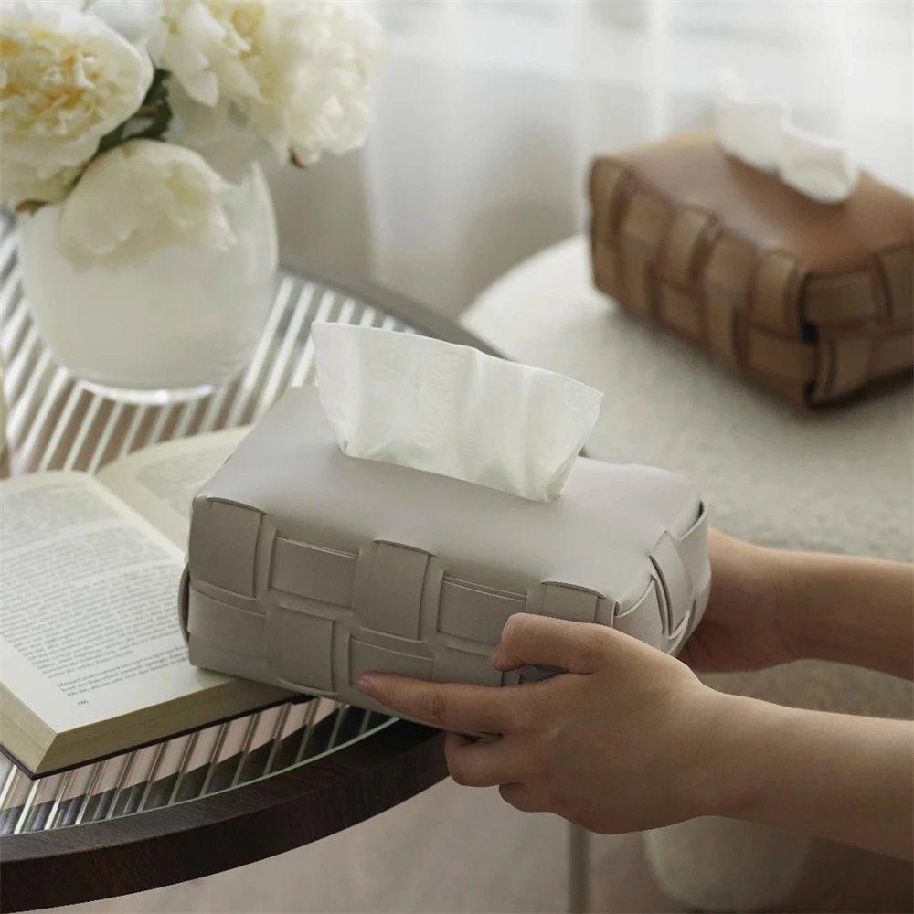 Greige woven tissue box held in hands on a glass side table