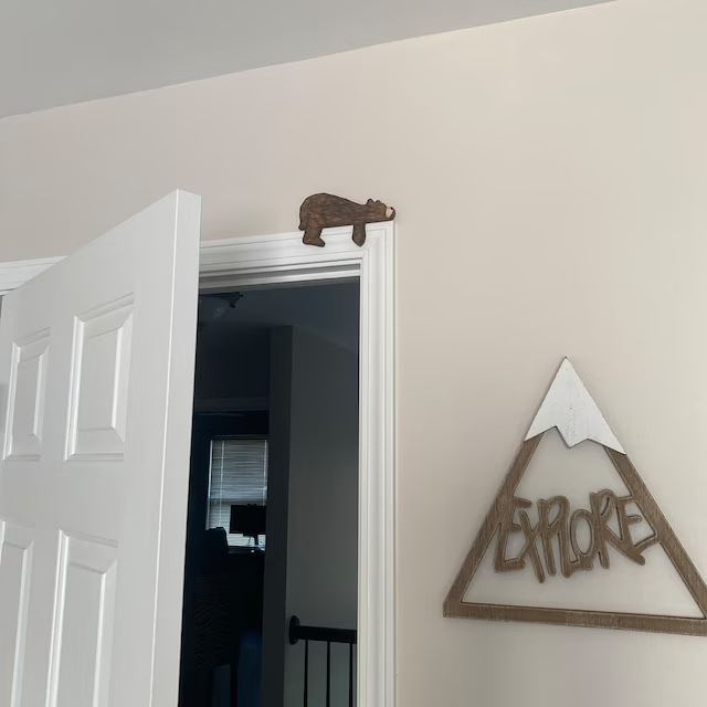 Carved wooden bear sitting on an open white door frame beside a mountain sign