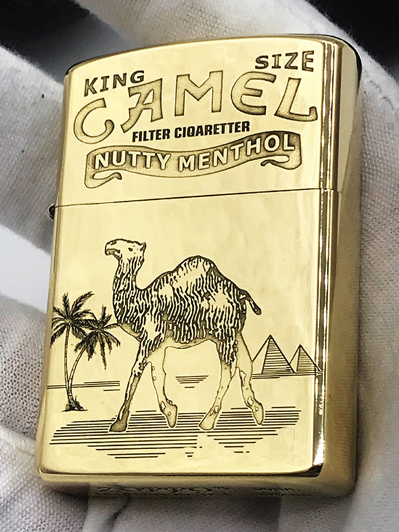Brass lighter held in hand showing the engraved front in use