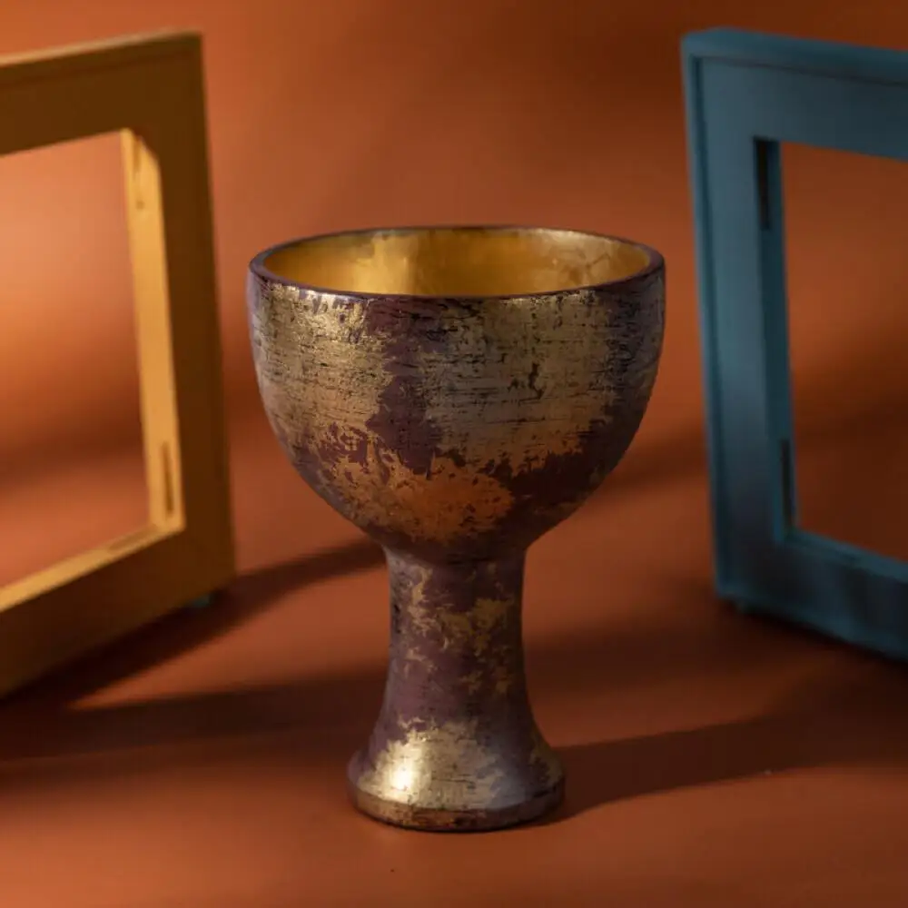 Holy Grail cup prop styled on a terracotta backdrop between picture frames