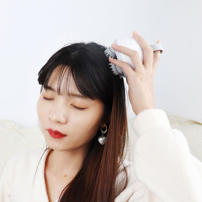 Woman with eyes closed massaging her scalp with a kneading head massager