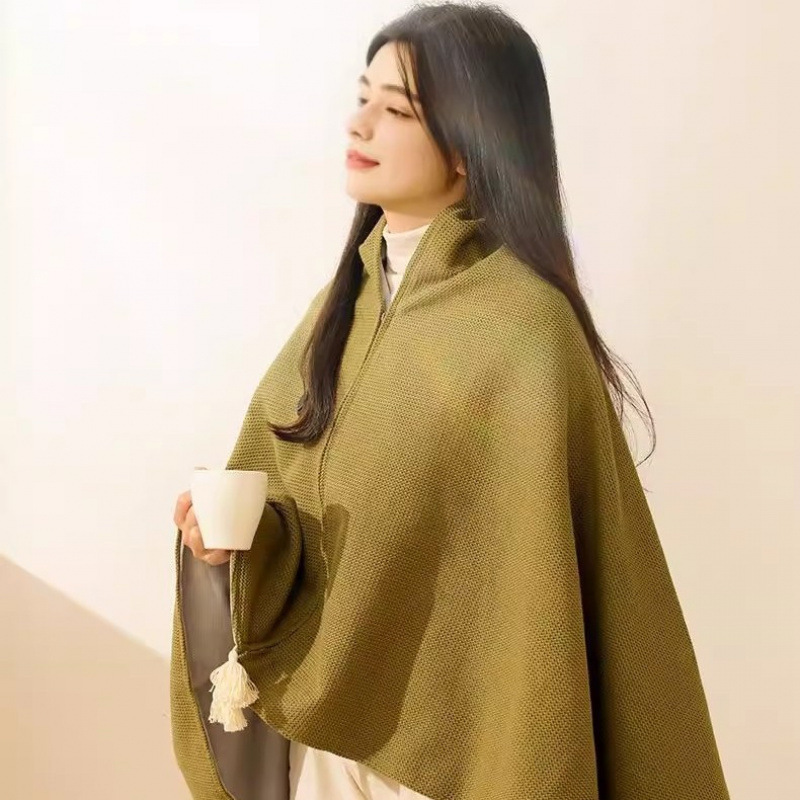 Woman in olive green knit heated shawl holding a mug by a sunlit wall
